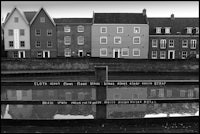a black and white photo of a row of houses next to a canal